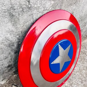 May include: A red, white, and blue Captain America shield. The shield has a red outer ring, a silver middle ring, and a blue center with a silver star. The shield is a circular shape.