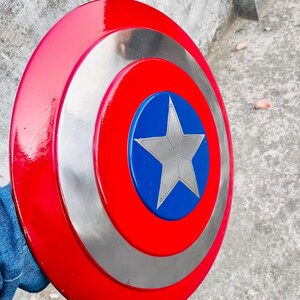 May include: A red, silver, and blue Captain America shield. The shield has a red outer ring, a silver middle ring, and a blue center with a silver star. The shield is round and appears to be made of metal.