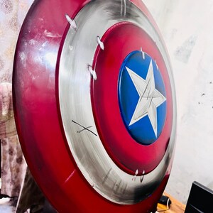 May include: A red, white, and blue shield with a star emblem. The shield has a circular design with a red outer ring, a silver middle ring, and a blue center with a white star. The shield has a distressed appearance.