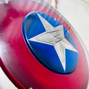 May include: A close-up of a shield with a red and silver outer ring, a blue center, and a large white star. The shield has a glossy finish and appears to be made of metal.