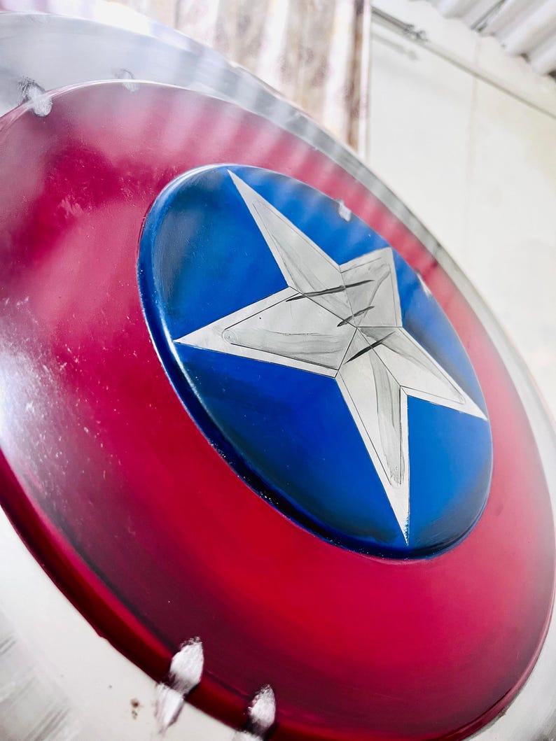 May include: A close-up of a shield with a red and silver outer ring, a blue center, and a large white star. The shield has a glossy finish and appears to be made of metal.