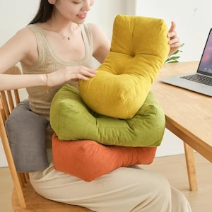 May include: Four colourful lumbar support cushions in yellow, green, orange, and grey. The cushions are made of a soft, textured fabric and are designed to provide back and posture support while sitting. The cushions are in a variety of shapes.