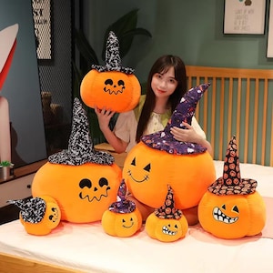 Puede incluir: Una colección de calabazas de peluche naranja con caras de jack-o'-lantern bordadas y sombreros de bruja negros. Los sombreros presentan varios diseños, incluyendo estrellas y diseños temáticos de Halloween. Estas calabazas decorativas son perfectas para Halloween.