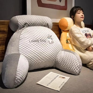 May include: A large, gray backrest pillow with a textured surface and a smaller headrest. The pillow features the text "Lovely Dog" and a dog graphic. The pillow is designed for comfort and support.