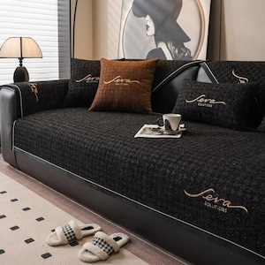 May include: A black sofa with a houndstooth pattern, complemented by brown and black cushions. The cushions and armrests display the embroidered text "Seva Solutions". A pair of fluffy slippers with a black and white design are on the floor.