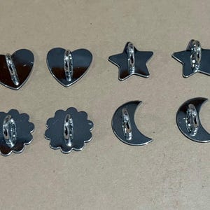 Puede incluir: Colección de ocho cortadores de galletas plateados en varias formas: dos corazones, dos estrellas, dos medias lunas y dos flores festoneadas. Cada cortador tiene un lazo de metal para colgar o guardar.
