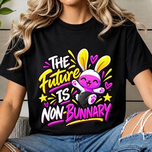 Pode incluir: Uma t-shirt preta com um gráfico de um coelho de desenho animado com pelo rosa e branco. O texto THE FUTURE IS NON-BUNNARY está em letras negrito amarelas, brancas e rosas, acentuado por estrelas amarelas e pequenos corações rosas.