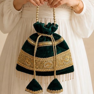 May include: A dark green velvet drawstring pouch bag featuring a gold beaded handle and a wide band of gold floral embroidery. The bag includes gold braided drawstrings with two matching velvet tassels at the ends and a fringe of gold beads.