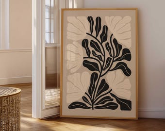 May include: A framed art print featuring a botanical design. The artwork showcases a central black plant with large, stylized leaves against a beige background. Soft, light beige floral shapes are subtly placed around the central plant. The frame is a warm, natural wood tone.