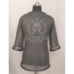 May include: A silver chainmail shirt with short sleeves, displayed on a mannequin. The shirt is made of small, interlocking metal rings, creating a flexible, protective garment. The sleeves end just below the elbow.