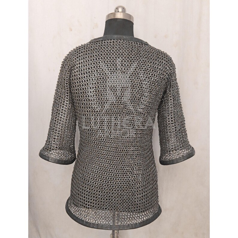 May include: A silver chainmail shirt with short sleeves, displayed on a mannequin. The shirt is made of small, interlocking metal rings, creating a flexible, protective garment. The sleeves end just below the elbow.