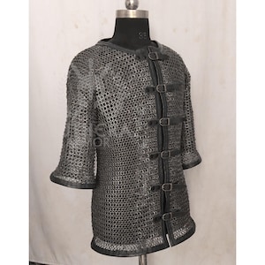 May include: A silver chainmail shirt with short sleeves and a leather trim. The shirt features leather straps with buckles down the front. The garment is displayed on a black mannequin.