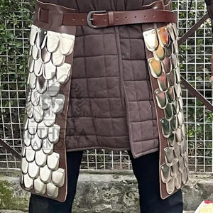 May include: A brown leather belt with a silver buckle and a brown leather apron with silver scale armor. The apron is attached to the belt and hangs down the legs. The armor is made of overlapping metal scales.