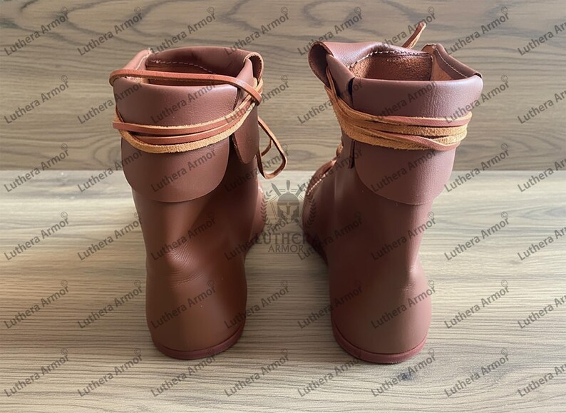May include: A pair of brown leather boots with a rolled-down cuff and leather laces. The boots are a reddish-brown colour and appear to be handmade. The boots are designed for historical reenactment or costume use.