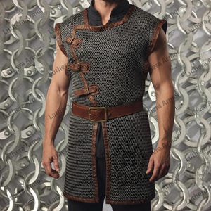 May include: A chainmail vest with brown leather detailing and straps. The vest includes a brown leather belt with a brass buckle. The chainmail is dark grey. The vest is worn over a black shirt.