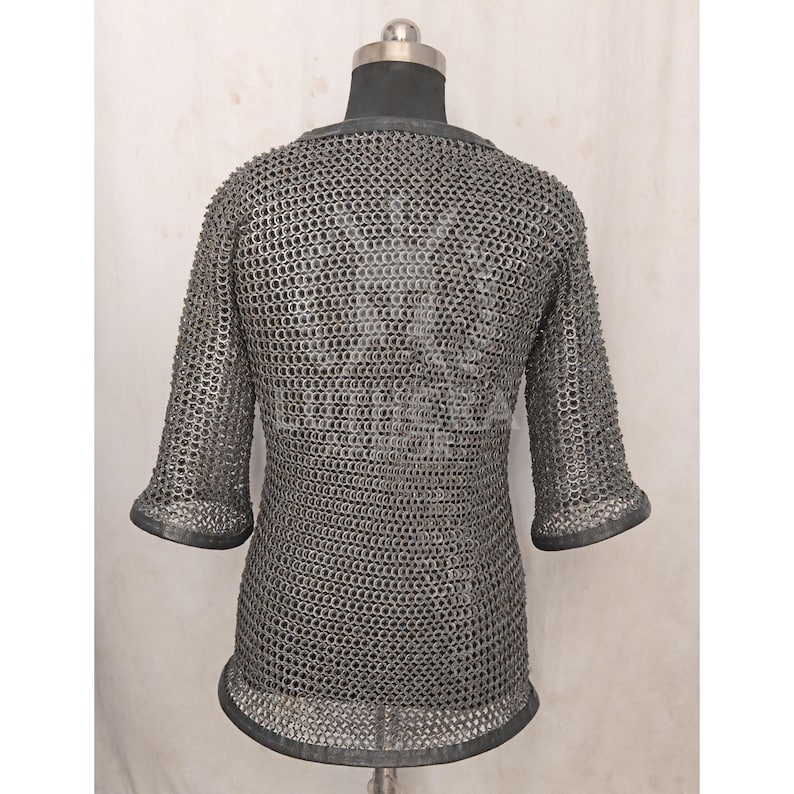 May include: A silver chainmail shirt with short sleeves, displayed on a mannequin. The shirt is made of small, interlocking metal rings, creating a flexible, protective garment. The sleeves end just below the elbow.