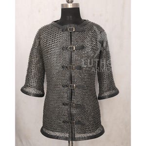 May include: A silver chainmail shirt with short sleeves and a leather collar and trim. The shirt has a series of leather straps with buckles down the front. The shirt is displayed on a mannequin.