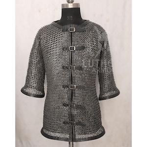 May include: A silver chainmail shirt with short sleeves and a leather collar and trim. The shirt has a series of leather straps with buckles down the front. The shirt is displayed on a mannequin.