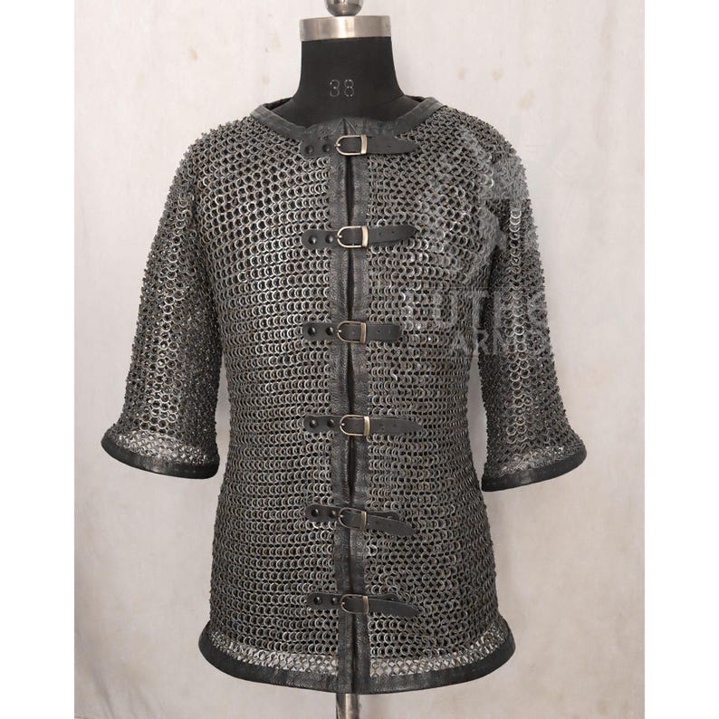 May include: A silver chainmail shirt with short sleeves and a leather collar and trim. The shirt has a series of leather straps with buckles down the front. The shirt is displayed on a mannequin.