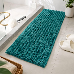 Op de afbeelding: Een rechthoekige, blauwgroene badmat met een getextureerd, ruig chenille-oppervlak met talloze kleine, verhoogde lussen. De mat heeft een consistente diepblauw-groene kleur en een platte, afgewerkte rand voor op de badkamervloer.