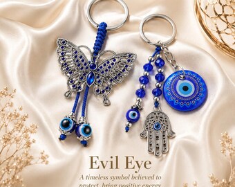 May include: Two keychains featuring blue evil eye beads. One keychain has a silver-toned butterfly with blue rhinestones and two dangling evil eye beads. The other has a blue evil eye disc, a silver-toned hamsa hand charm, and blue beads.