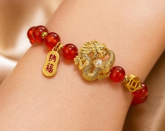 May include: A gold-colored bracelet featuring a detailed dragon design with a pearl accent. The bracelet includes red beads and a gold charm with Chinese characters. A gold coin-shaped bead is also present.