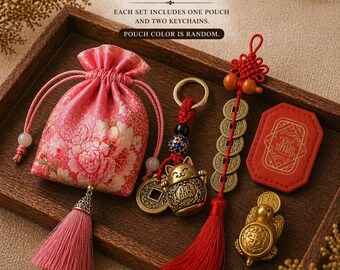 May include: A gift set featuring a pink floral drawstring pouch with a tassel, a keychain with a brass cat charm and coins, a long red tassel keychain with brass coins, and a red rectangular charm with a small brass turtle figurine.