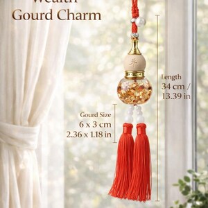 May include: A hanging gourd charm with a red cord, a wooden top section, and a clear glass base filled with gold-colored flakes. It features white beads and two red tassels. Total length is 13.39 inches, with a gourd size of 2.36 by 1.18 inches.