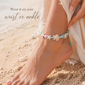 Può includere: Braccialetto alla caviglia con stelle marine bianche, una tartaruga e perline blu e rosa. Il braccialetto è su un cordino blu. Il testo "Wear it on your wrist or ankle" è nell'immagine.