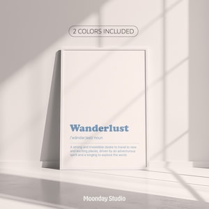 May include: White framed print with the word "Wanderlust" in blue, along with its definition. The print includes the text "2 COLORS INCLUDED" and "Moonday Studio". The print is leaning against a white wall.