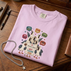 May include: A light pink t-shirt featuring a graphic of several seagulls with speech bubbles containing the text "YOU ROCK!", "SO COOL!", "THANK YOU!", "YOU'RE AWESOME!", and "TEACHER!", along with a sign that reads "Teacher Name BEST TEACHER EVER!"