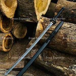 May include: A katana sword with a black handle and scabbard rests on a pile of wood logs. The blade has a patterned design. The sword is a traditional Japanese weapon, often used in martial arts and historical reenactments.