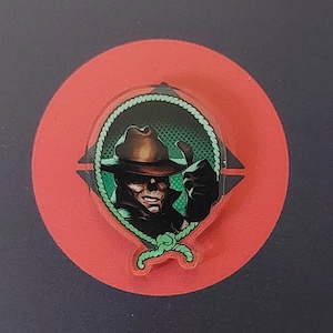 Könnte beinhalten: Eine grün-schwarze illustrierte Figur, die einen braunen Cowboyhut und einen grünen Schal trägt. Die Figur trägt eine schwarze Jacke und hat ein grünes Seil um den Hals.