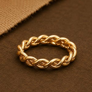 Op de afbeelding: Een goudkleurige ring met een doorlopend gedraaid touwontwerp. De band bestaat uit meerdere in elkaar grijpende strengen die een getextureerd, gevlochten uiterlijk creëren met een gepolijste, reflecterende afwerking over de gehele cirkelvormige structuur.