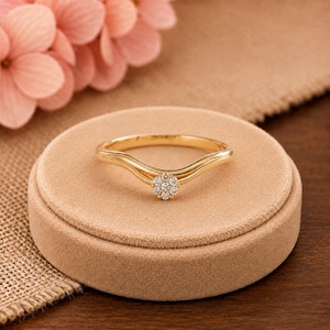 Op de afbeelding: Een gouden ring met een delicate, gebogen band die in het midden afloopt. Het middelpunt is een kleine, ronde cluster van zeven piepkleine, heldere, fonkelende steentjes in een bloemvorm, stevig gezet in het gepolijste gouden metaal.