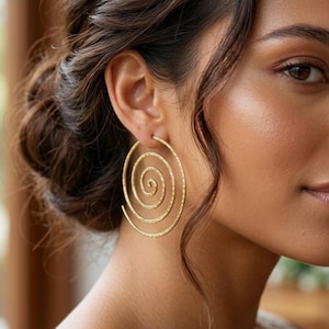 May include: A gold-toned hoop earring featuring a spiral design. The earring has a textured surface and is shaped like a continuous coil that starts from the centre and expands outwards in a circular pattern, hanging from the earlobe.
