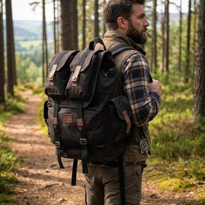 Może przedstawiać: Ciemnobrązowy płócienny plecak z wieloma kieszeniami i skórzanymi akcentami. Plecak ma regulowane paski i klamry. Osoba ma na sobie koszulę w kratę, kamizelkę i spodnie cargo, idąc leśną ścieżką.