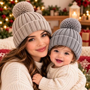 May include: Two matching beige knit beanies with large pom-poms on top. Each hat features a thick ribbed cuff and a soft, textured knit pattern. The beanies are designed with a classic rounded shape and a prominent pom-pom detail.