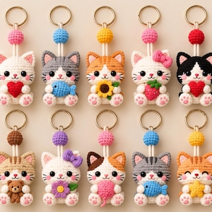 May include: A collection of ten handmade crochet cat keychains, each featuring a unique accessory such as a heart, fish, sunflower, strawberry, bow, teddy bear, flower, or star. Each cat has a round head, small ears, and a gold-toned metal ring.
