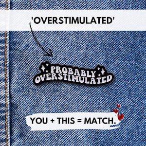 May include: A black and white enamel pin with the text "Probably Overstimulated" in a stylized font, set against a denim background. The pin is accompanied by the text "YOU + THIS = MATCH."