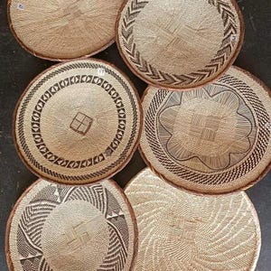 Pode incluir: Uma coleção de seis cestos redondos tecidos com padrões intrincados. Os cestos apresentam tons naturais de bege e castanho, com bordas decorativas e desenhos geométricos. Adequados para decoração de casa ou armazenamento.