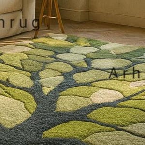 May include: A green and beige area rug with a tree design. The rug features a dark gray trunk and branches, with leaf-shaped patterns in various shades of green and beige. The rug is on a wooden floor.