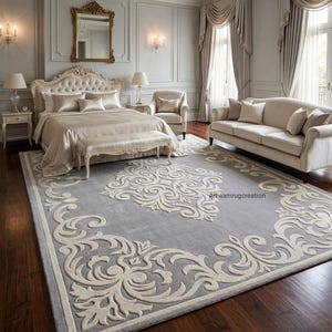 May include: A large rectangular area rug featuring a light gray base with an intricate cream-colored scrollwork pattern and a matching border. The rug displays the text Arhaamrugcreation in small black letters on its surface.