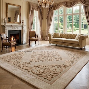 May include: A large rectangular area rug featuring a beige background with a raised, darker beige damask pattern in the centre and along the borders. The rug displays the text Arhaamrugcreation in the lower left corner of the patterned area.