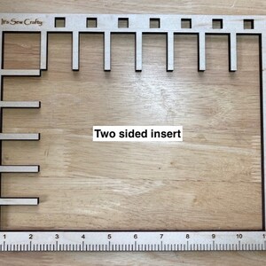Puede incluir: Una herramienta de costura de madera con un marco rectangular y varias formas recortadas. La herramienta tiene una regla a lo largo del borde inferior, marcada de 1 a 11 pulgadas (aproximadamente 28 cm). El texto "It's Sew Crafty" y "Two sided insert" son visibles.