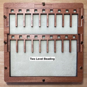 Puede incluir: Un tablero de abalorios de madera de dos niveles con un interior verde claro. El tablero tiene un marco rectangular con herrajes de lat&oacute;n y el texto "Two Level Beading". El marco es de madera marr&oacute;n oscuro.