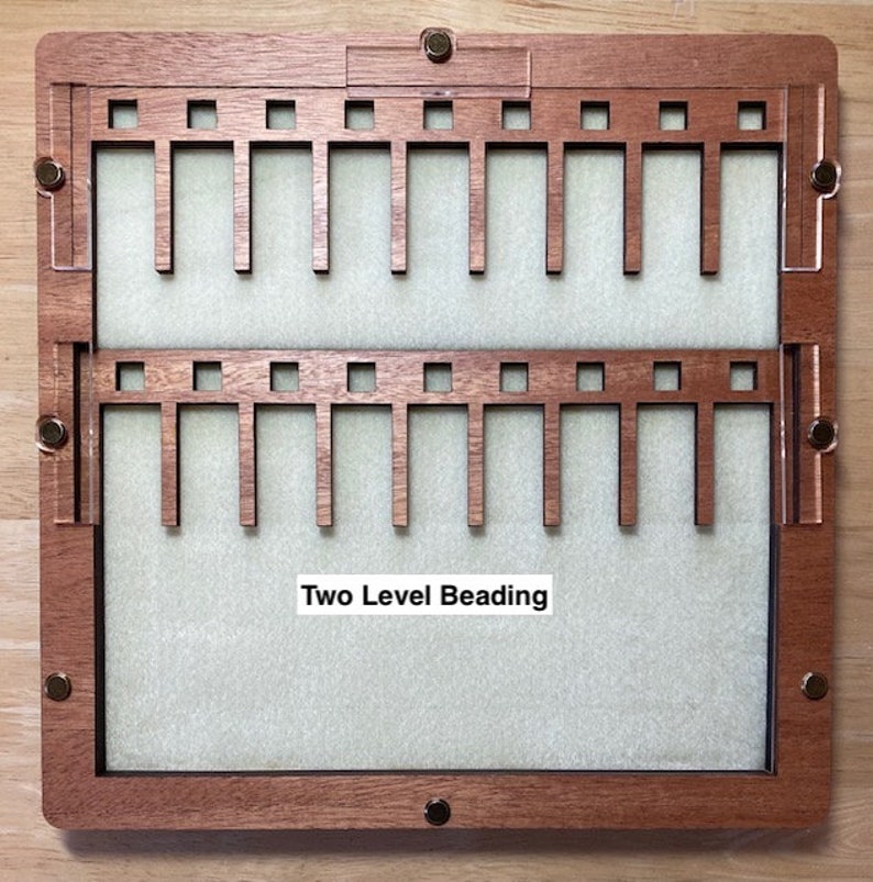 Puede incluir: Un tablero de abalorios de madera de dos niveles con un interior verde claro. El tablero tiene un marco rectangular con herrajes de lat&oacute;n y el texto "Two Level Beading". El marco es de madera marr&oacute;n oscuro.