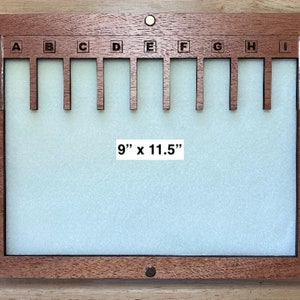 Puede incluir: Un tablero de exhibici&oacute;n de madera con un interior verde claro y un marco marr&oacute;n oscuro. El tablero tiene nueve ranuras etiquetadas de la A a la I. El texto "9" x 11.5" (22,86 cm x 29,21 cm) es visible.