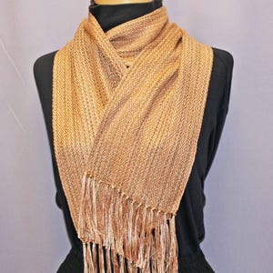 Puede incluir: Bufanda tejida en tonos dorados y beige, con un dise&ntilde;o de rombos. La bufanda tiene un borde con flecos y est&aacute; drapeada sobre un maniqu&iacute; negro. Este accesorio es adecuado para a&ntilde;adir calidez y estilo.