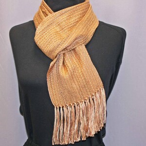 Puede incluir: Bufanda tejida en tonos dorados y marrones, exhibida en un maniqu&iacute; negro. La bufanda presenta un patr&oacute;n de diamantes y flecos en los extremos. La bufanda est&aacute; hecha de un material suave y texturizado. Mide unos 170 cm.
